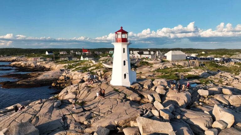 A scenic view of Peggy's Cove lighthouse surrounded by rocky shores and quaint houses under a blue sky with clouds