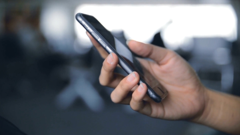 A person is holding a smartphone, ensuring it is updated while in a public space