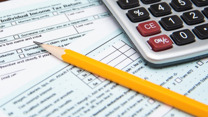 Pencil and calculator placed on tax forms used for tracking income and keeping records accurately