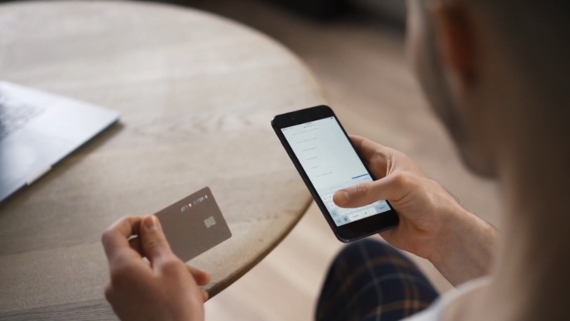 Person checking bank deposits on a smartphone while holding a credit card
