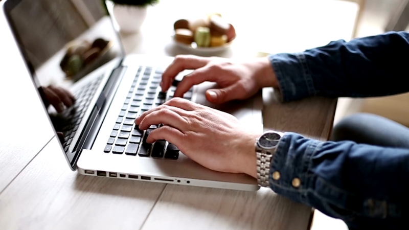 A person types a legal letter on a laptop at a wooden table near a plate of snacks