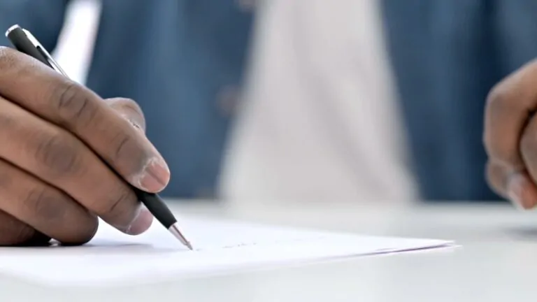 A person writes a legal letter by hand on a sheet of paper at a desk