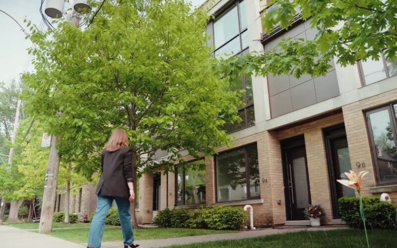 A woman walks along the sidewalk in front of a building, dressed casually and enjoying her surroundings