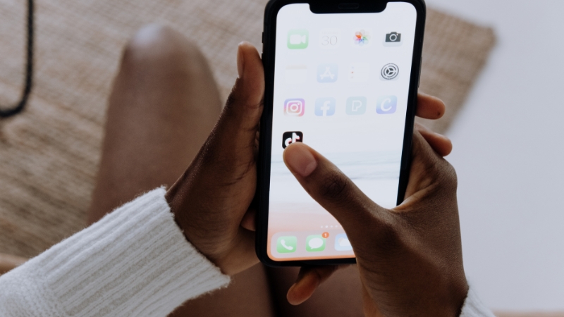A person holds a smartphone and taps the TikTok app