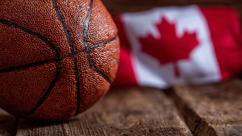 A basketball rests on a wooden surface with a Canadian flag in the background