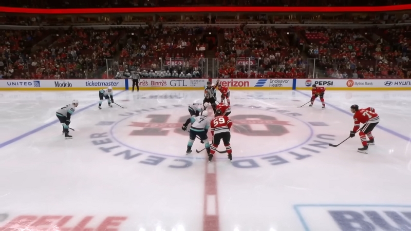 Players line up at center ice for an NHL faceoff in a packed arena