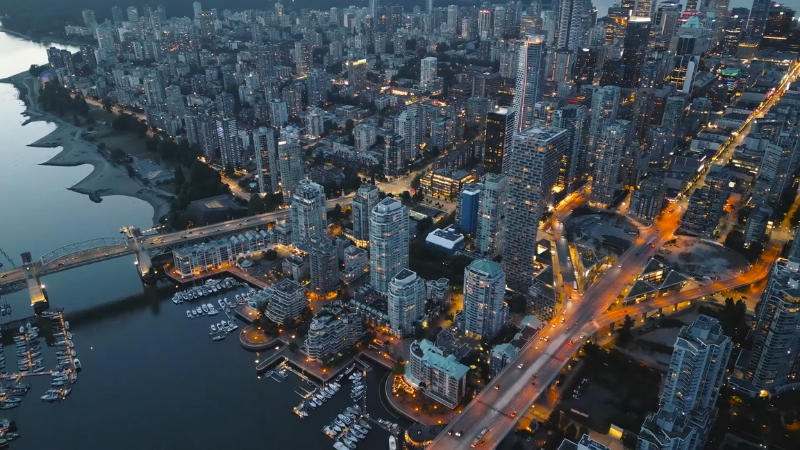 An evening aerial view shows a busy city skyline with illuminated streets near the water