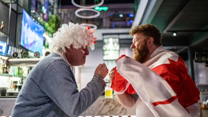 Two Canadian fans cheer and argue playfully at a bar during a game night
