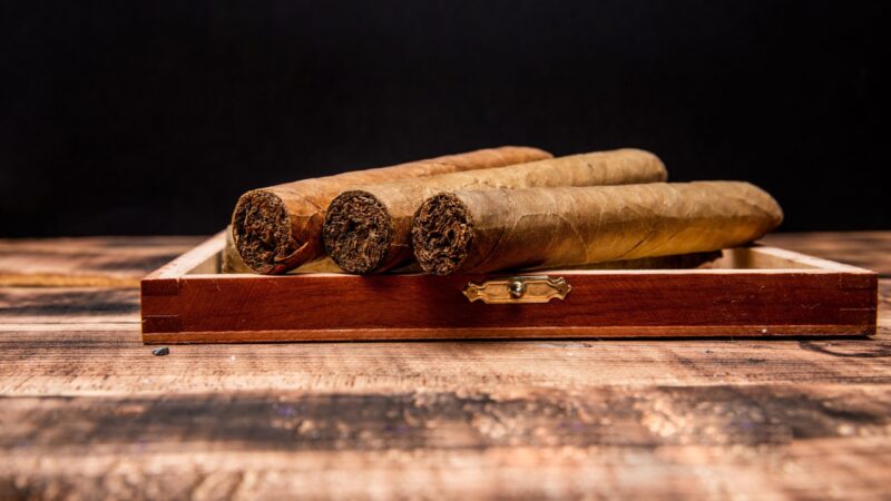 Cuban cigars rest inside an open wooden cigar box.